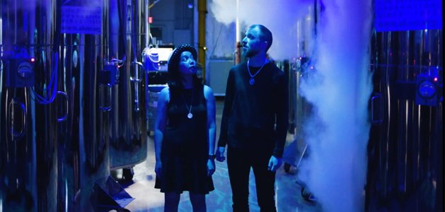 Carrie and Witek Radomski standing between cryogenic dewars in blue light